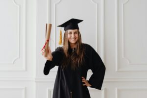 Smiling young woman in graduation attire holding diploma, showcasing academic success.